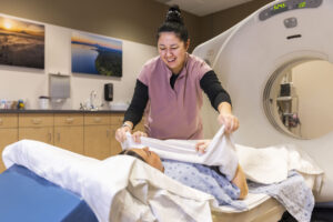 Female CT technologist covering a patient on the table with a blanket.